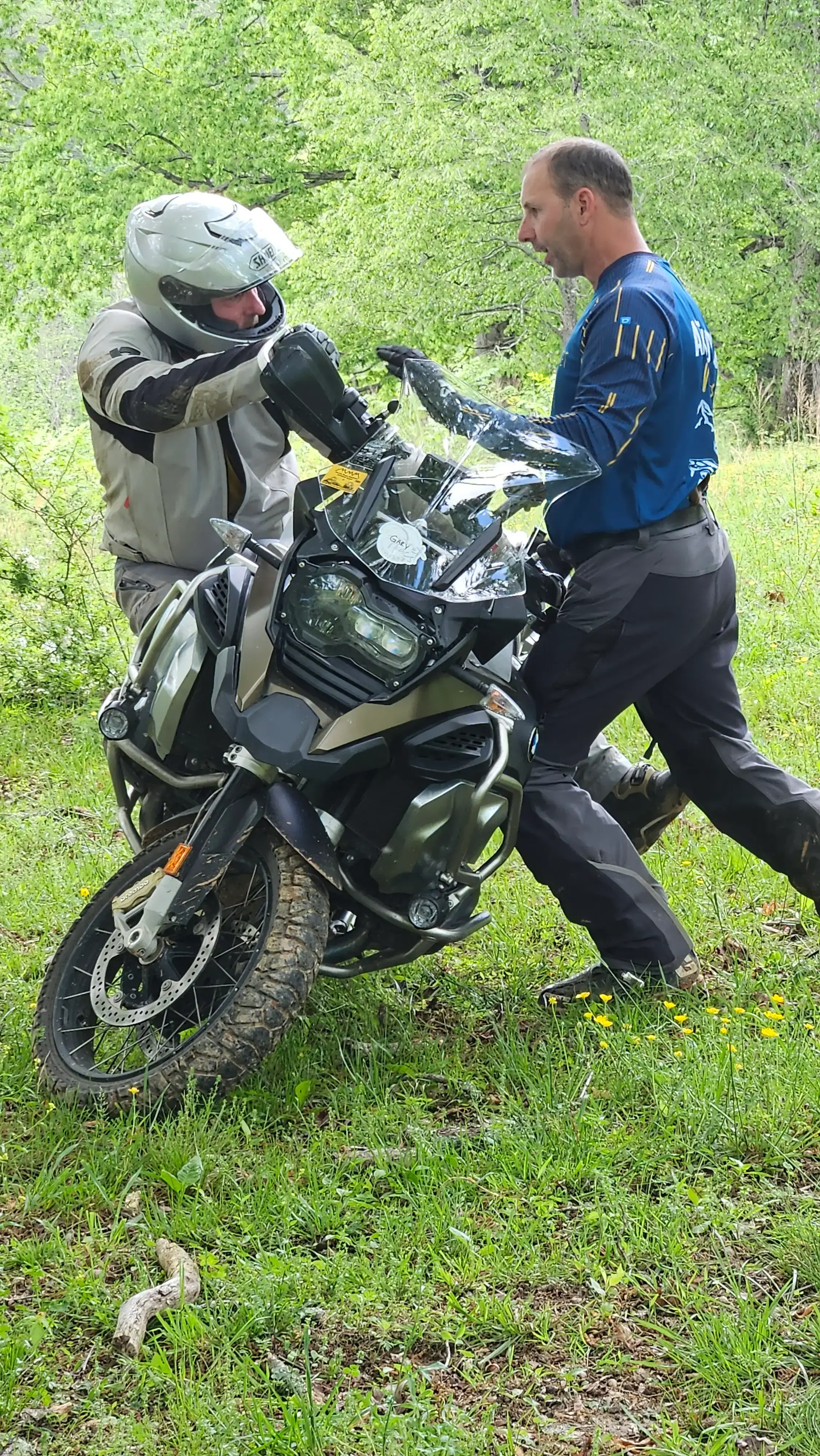 Bret Tkacs gives a student hands-on coaching beside a large adventure bike on a grassy slope