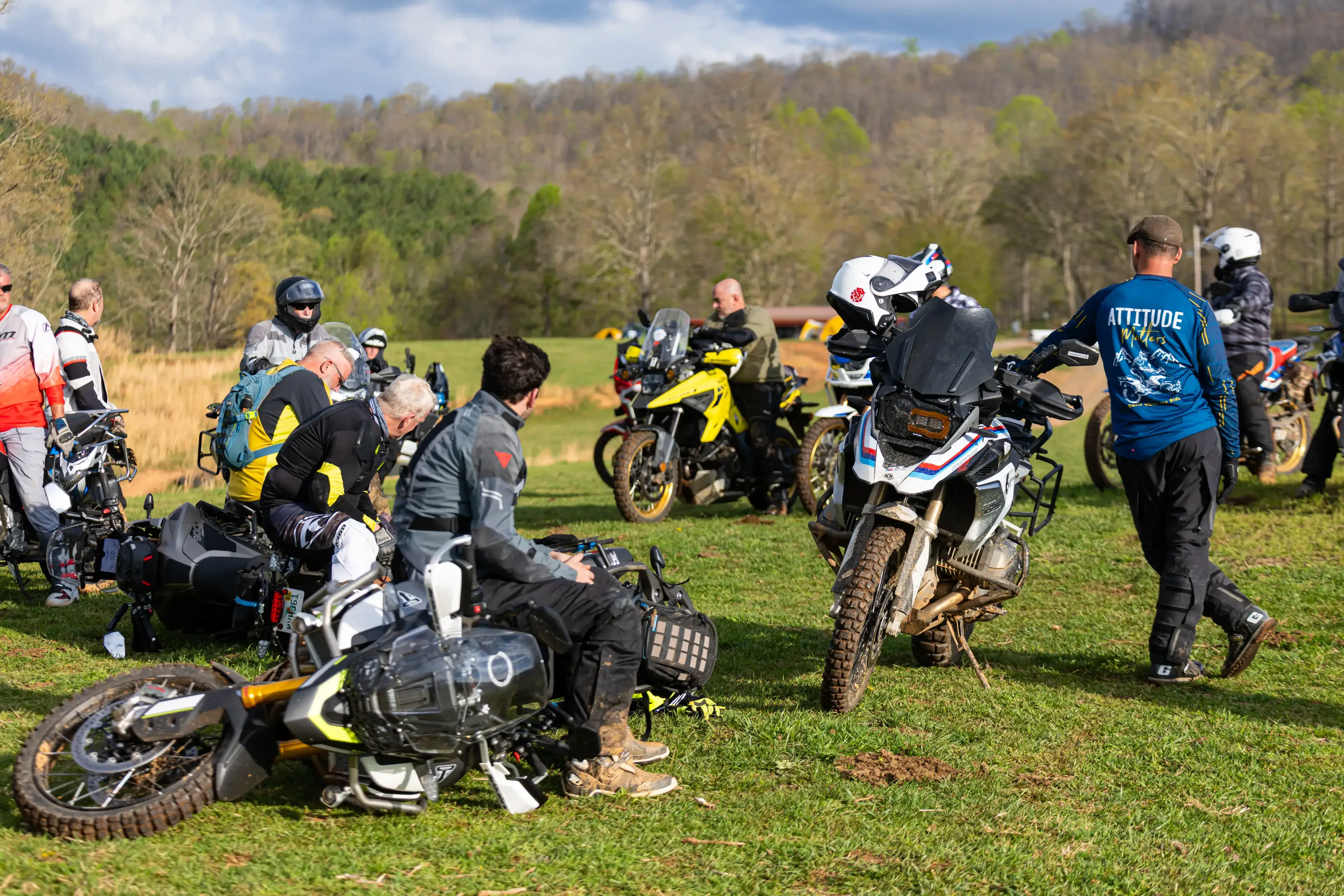 Riders and their adventure bikes gather on a grassy field during class, wooded hills behind, Georgia
