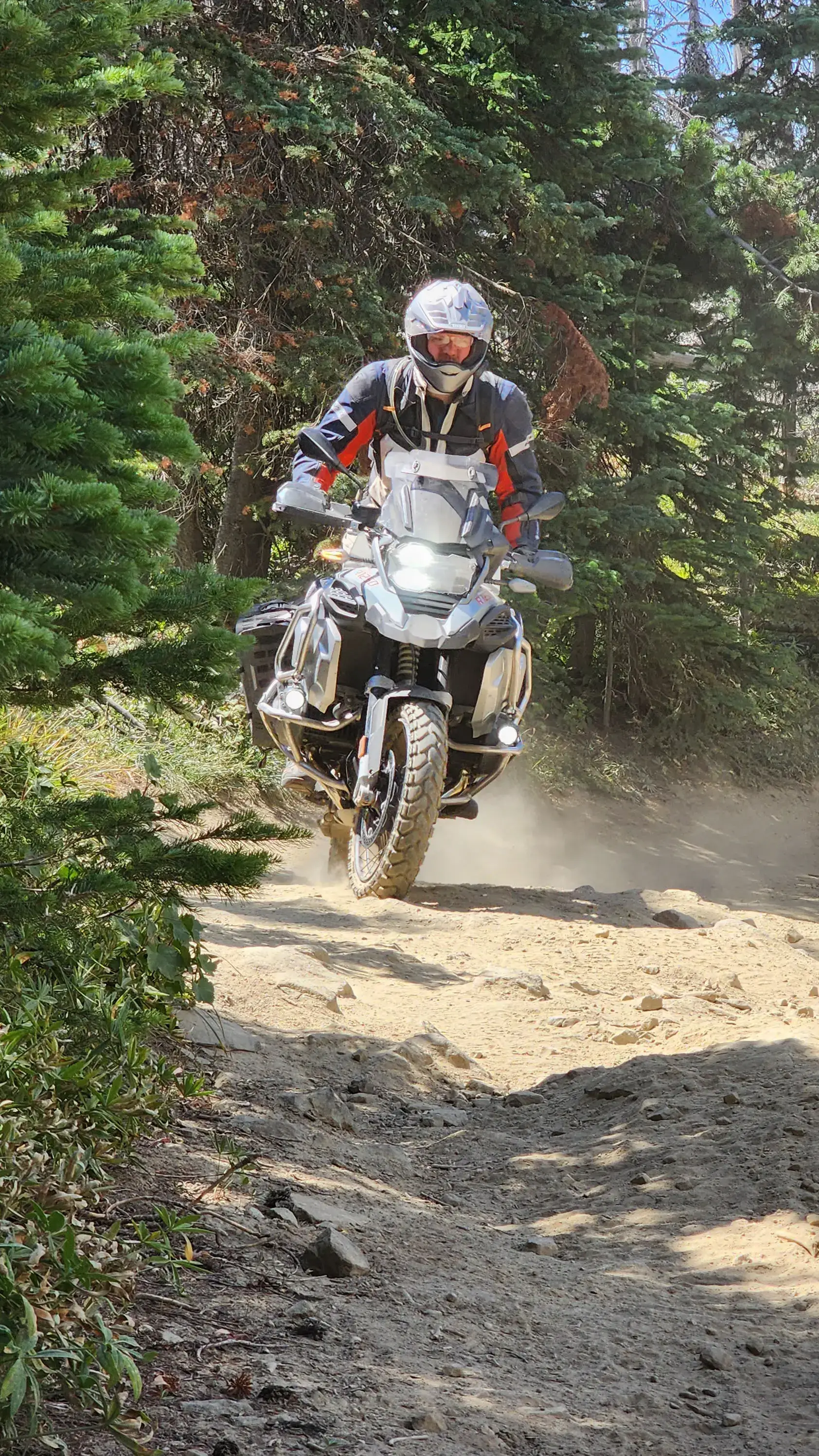 A student on a BMW adventure bike rounds a dusty, rocky forest trail, Washington Backcountry Discovery Route
