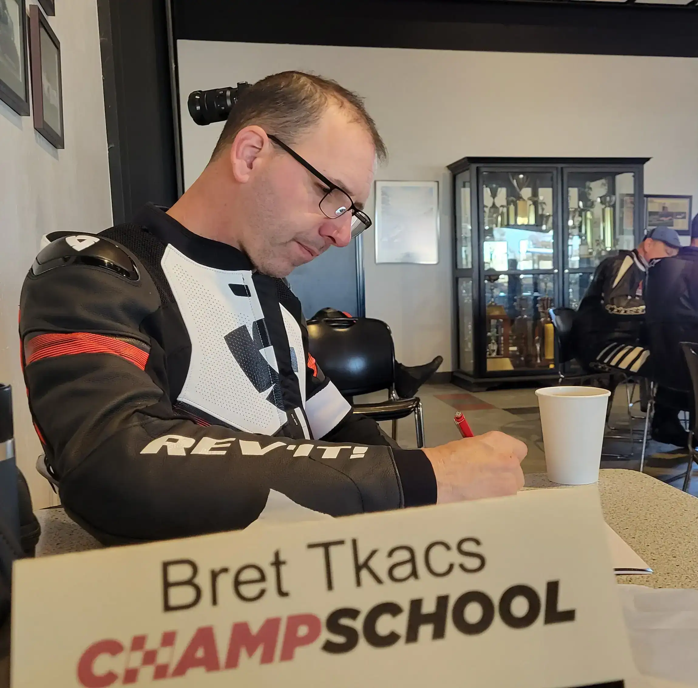 Bret Tkacs, in riding gear, takes notes in a classroom at the Yamaha Champ School