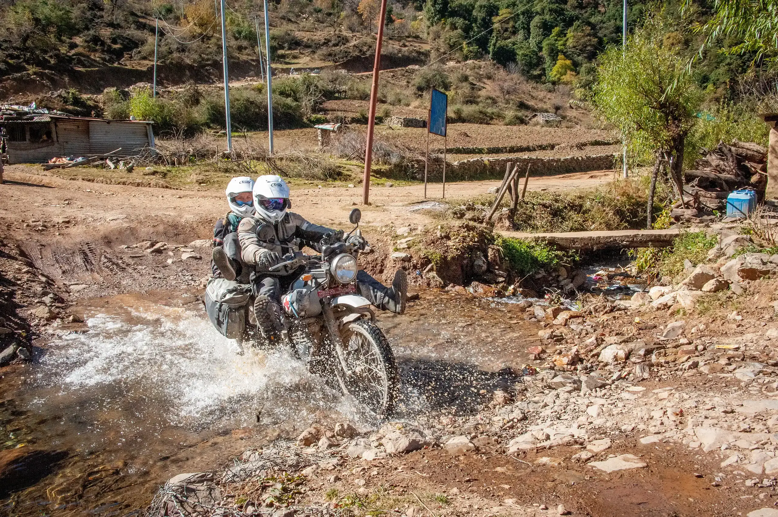 Bret Tkacs splashes through a village stream crossing with a passenger on the back, Nepal