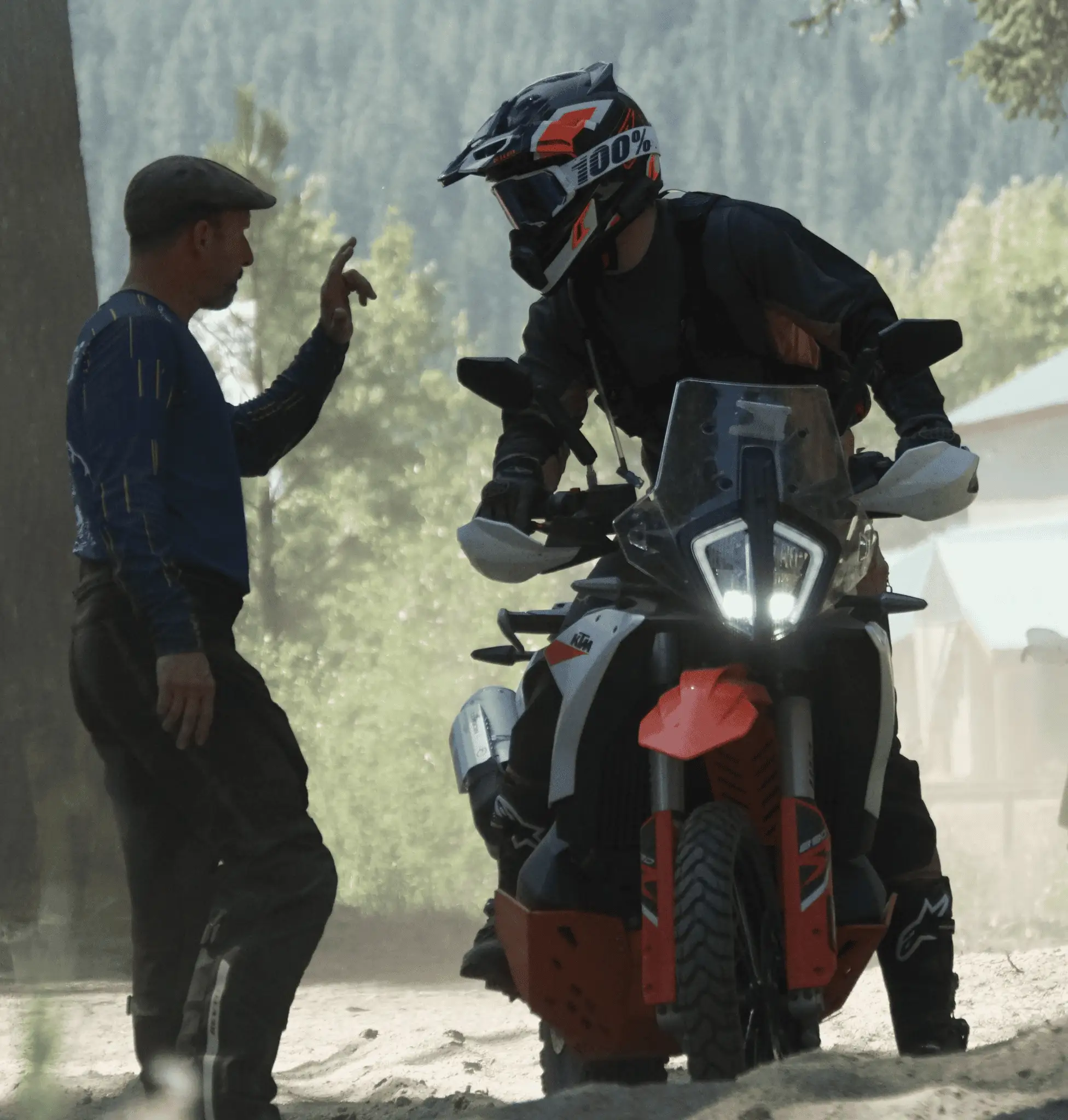 Bret Tkacs signals to a rider on a KTM in a dusty forest clearing, Washington