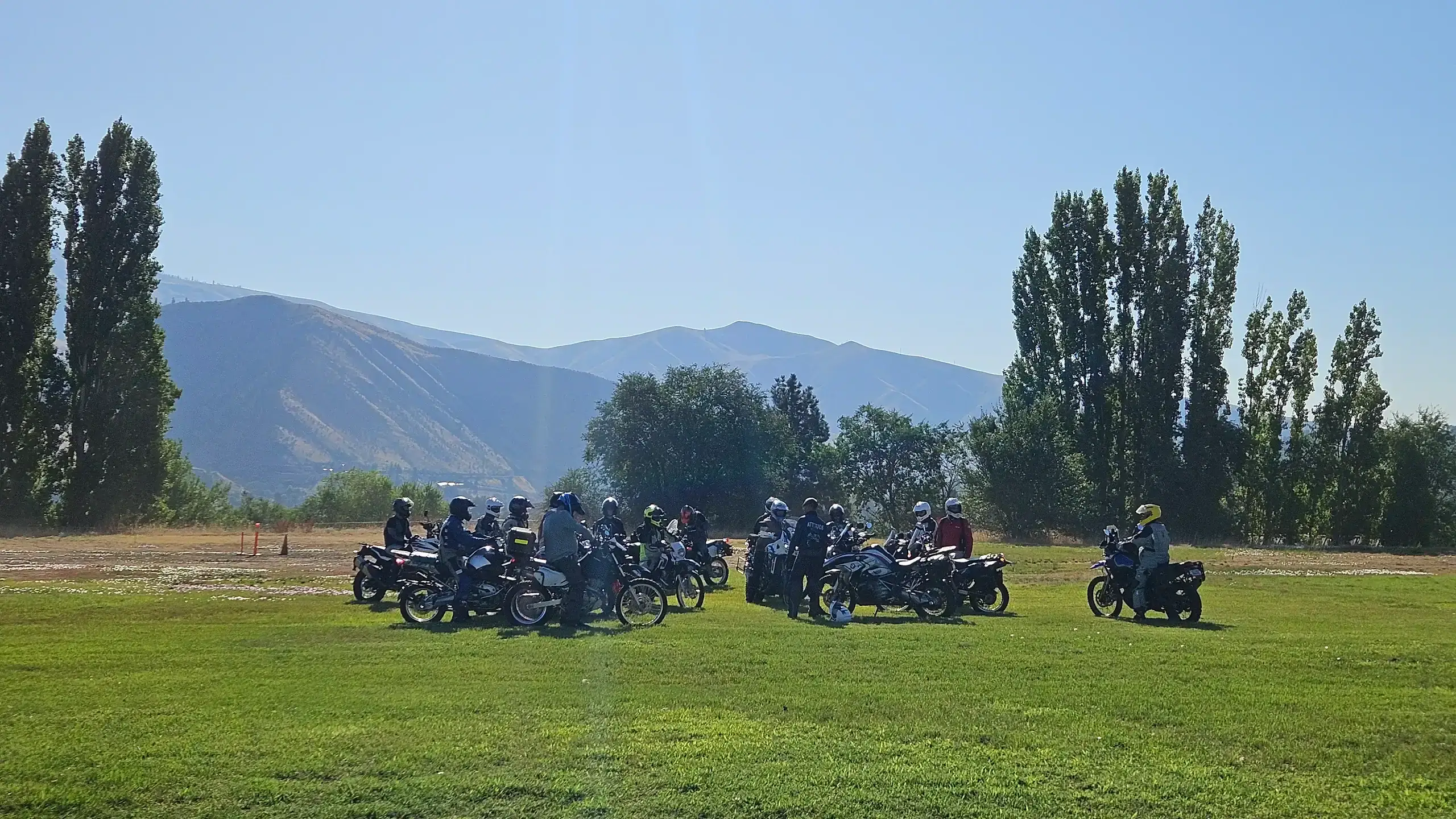 Riders gather on their bikes in a grassy field below dry mountains, Washington